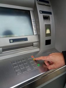 Man's using the ATM machine with cash cards and entering PIN/pass code on keypad.